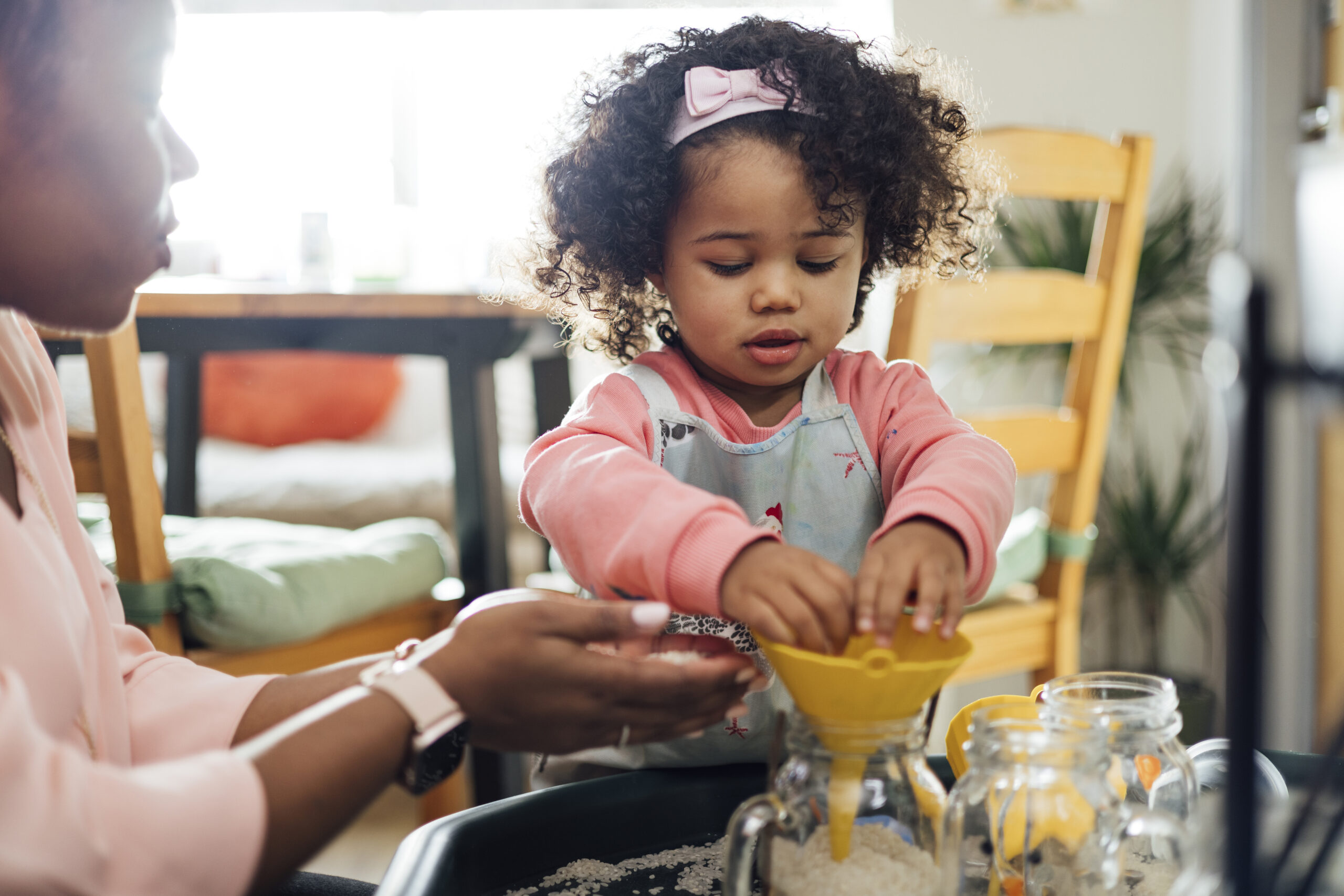 Child doing a funnel-and-jars activity with a parent at the kitchen table