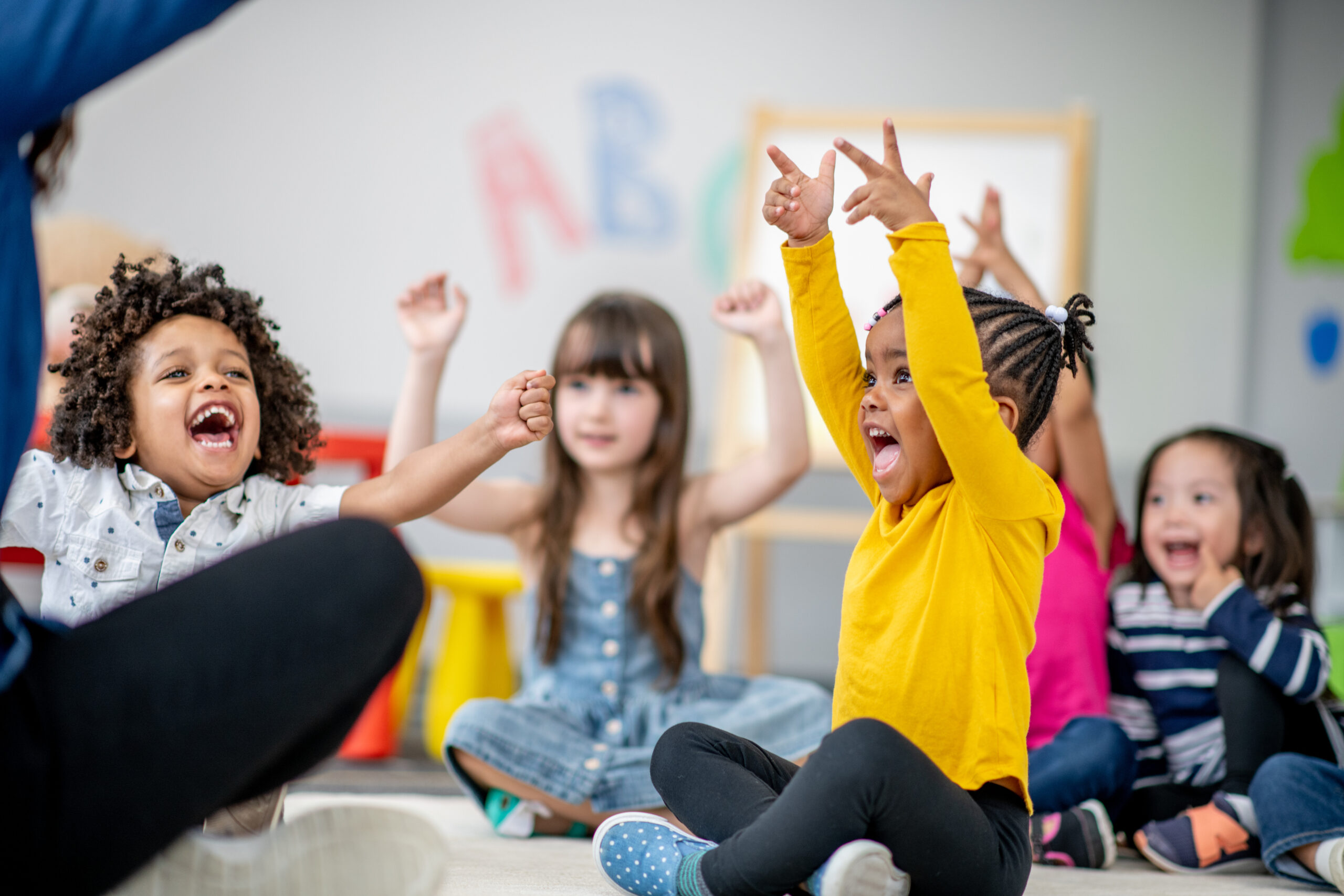 Children in kindergarten classroom raising hands during activity