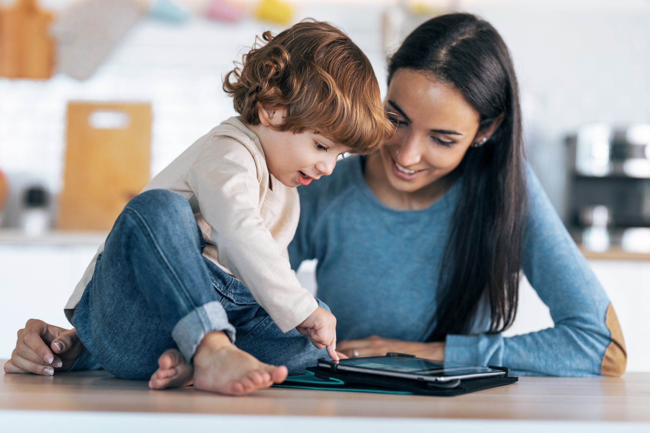 Mother and toddler using an educational app on a tablet at home, tapping and learning together.