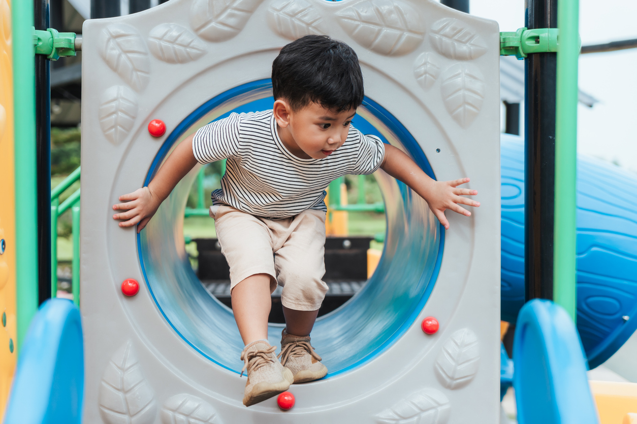 Preschool boy crawling through a tunnel on a playground, building confidence and motor skills during outdoor play.