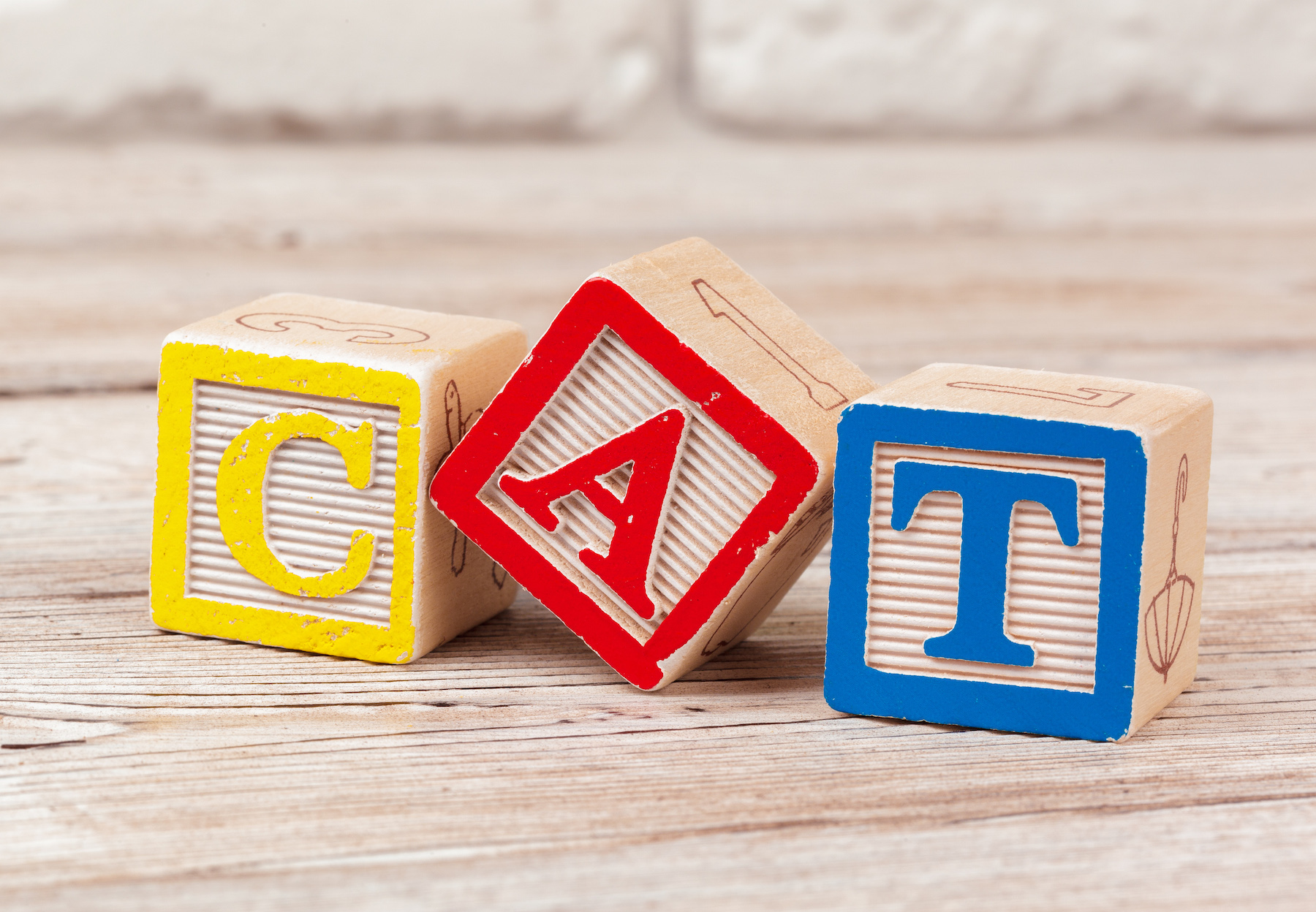 Three wooden blocks with colorful borders spell "CAT" in yellow, red, and blue letters, arranged on a wooden surface.