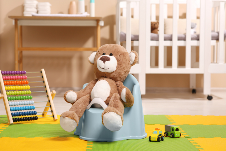 Cute teddy bear sitting on a light blue baby potty during toilet training.