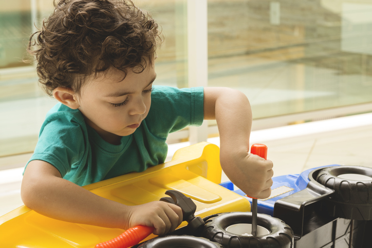 Preschool child using a toy screwdriver to fix a toy truck, practicing problem-solving and fine motor skills through play