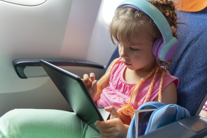 A girl wearing headphones watches in-flight entertainment on an airplane, illustrating a parent allowing screen time during travel.