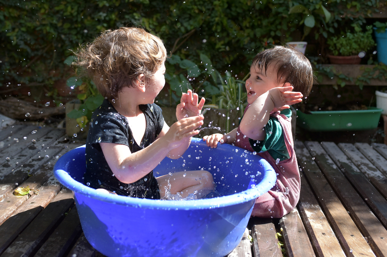 Siblings playing together with water during an outdoor water play activity.