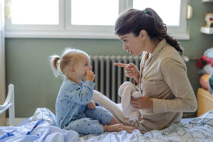 A mother talks calmly to her crying toddler in pajamas, showing loving and firm discipline.