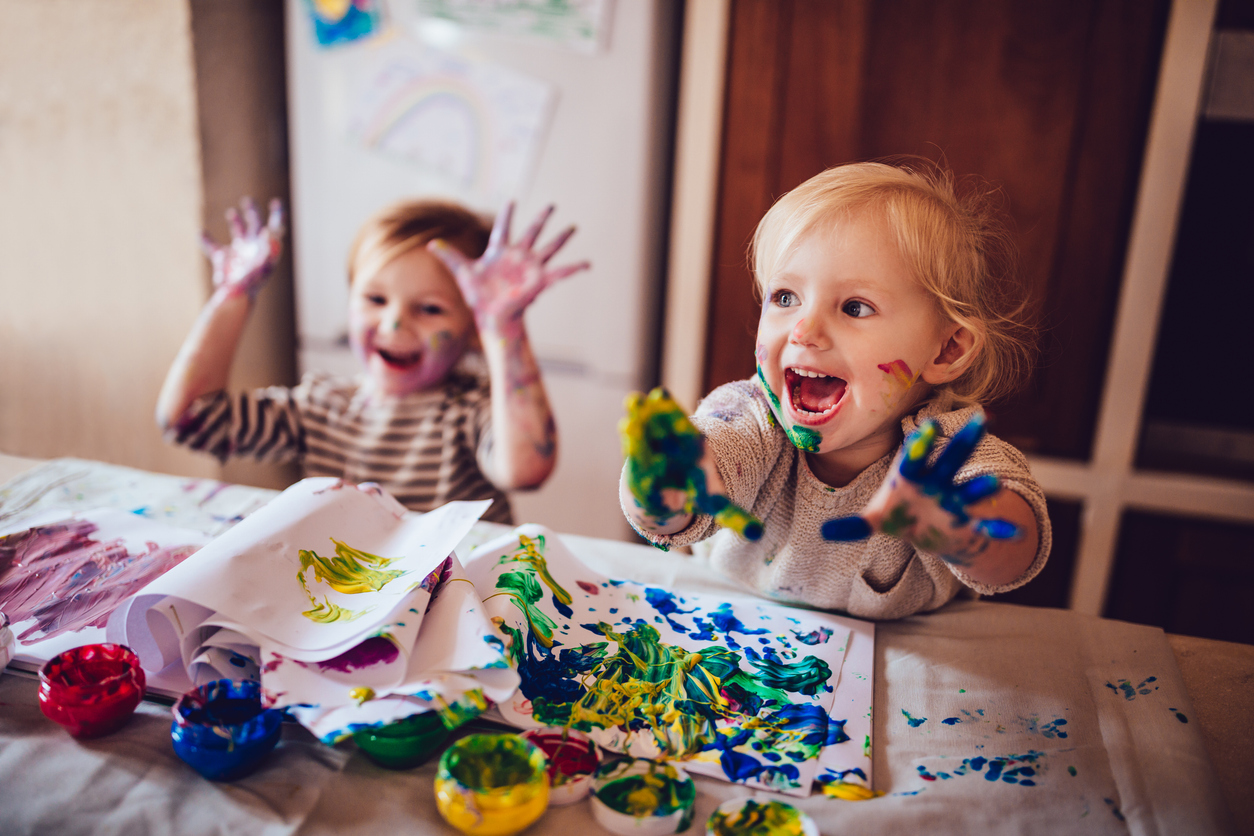 Happy young girls with paint-covered hands and faces joyfully finger painting together, expressing creativity and having fun.