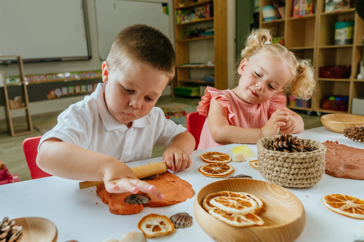 Young children using clay and natural materials during a hands-on activity that supports gross motor skill development.