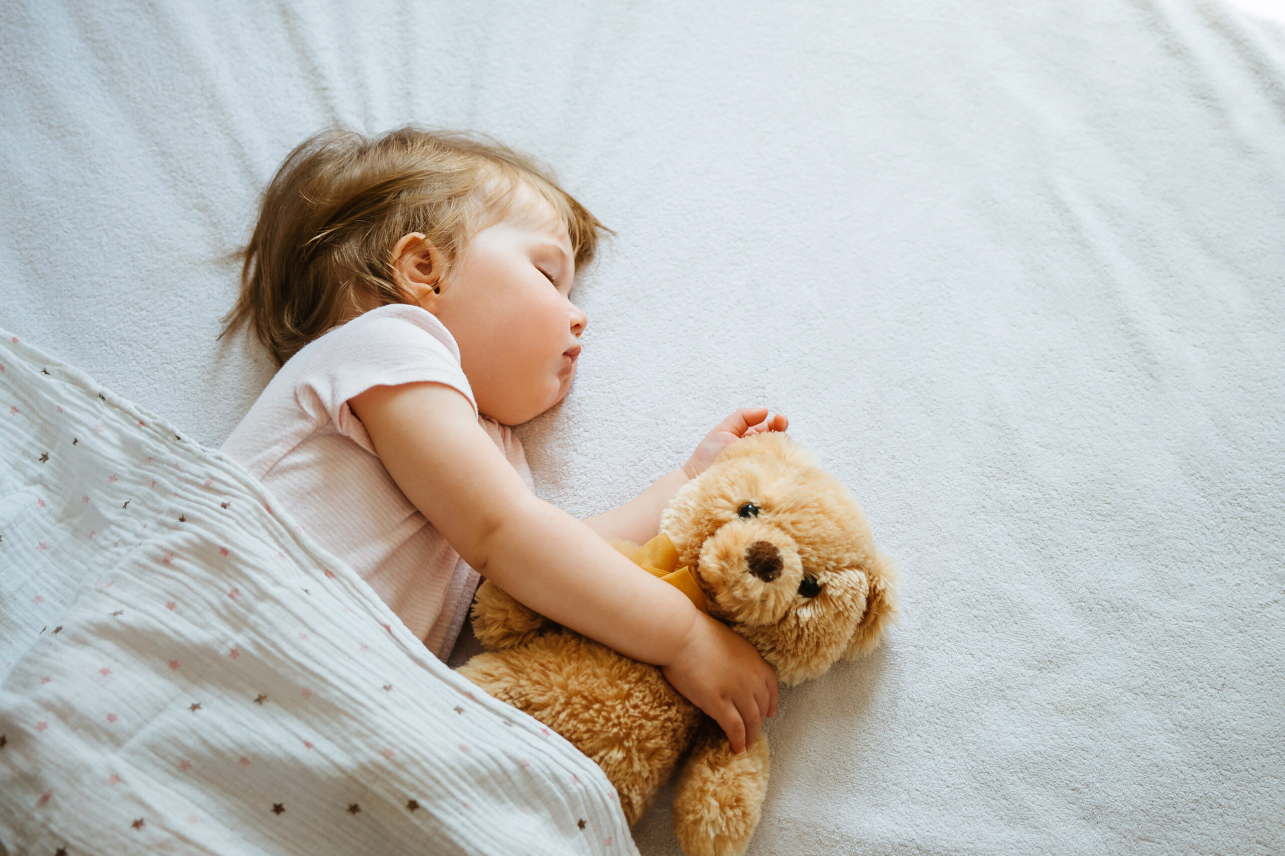 Toddler sleeping in bed hugging a teddy bear
