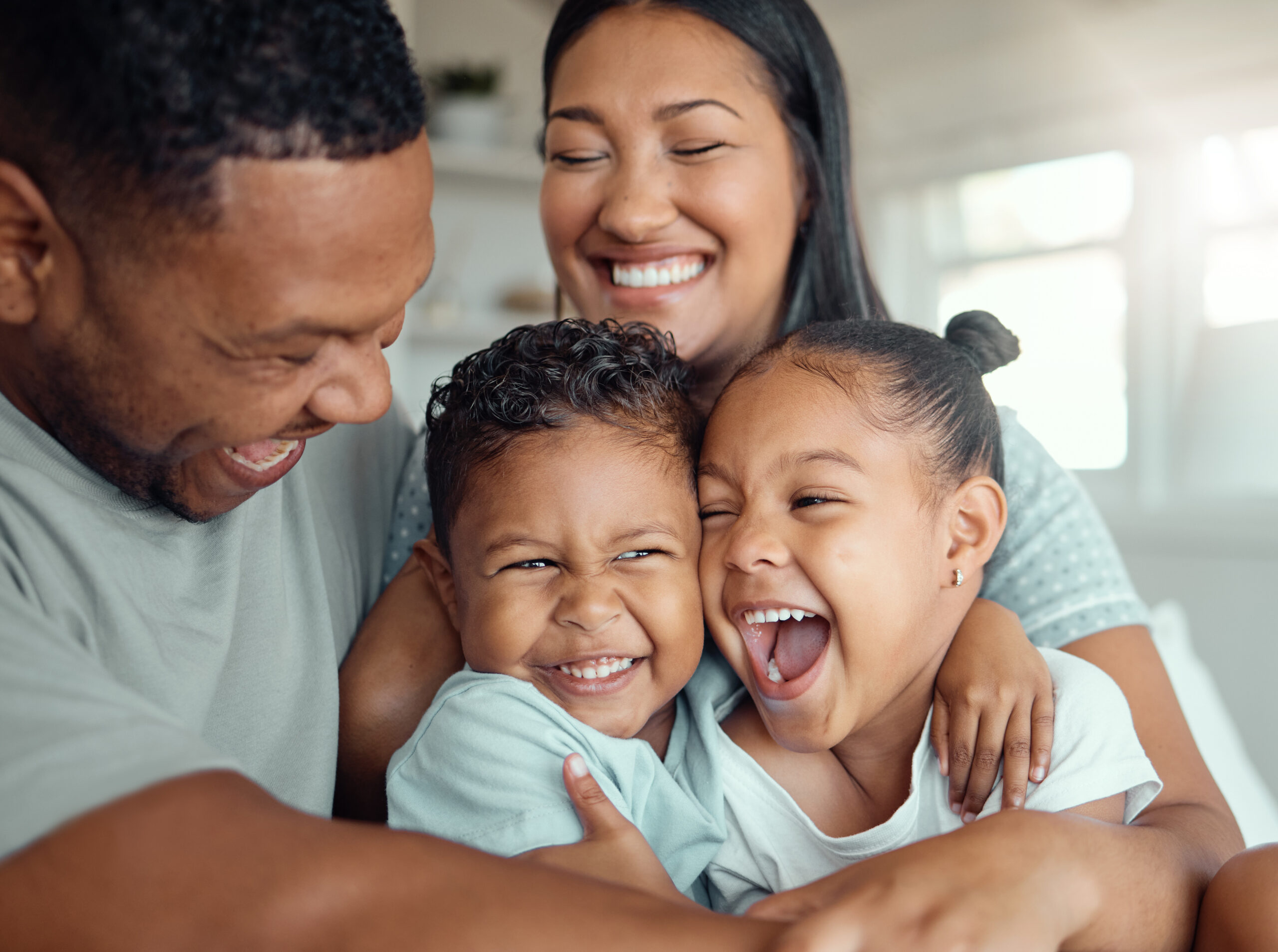 Happy family of four laughing and hugging together at home — parents and two young children sharing a joyful moment