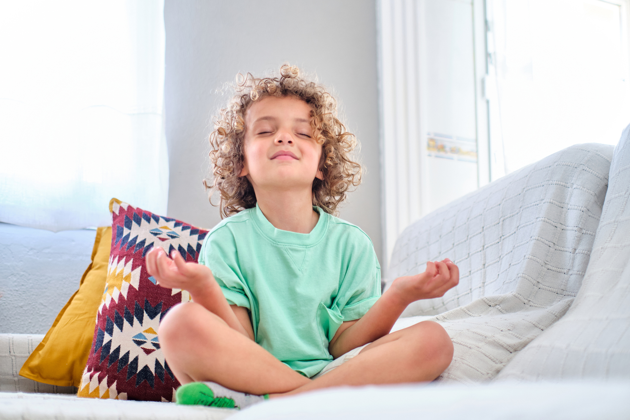 Child sitting cross-legged on a sofa with eyes closed, practicing mindfulness and calm breathing at home