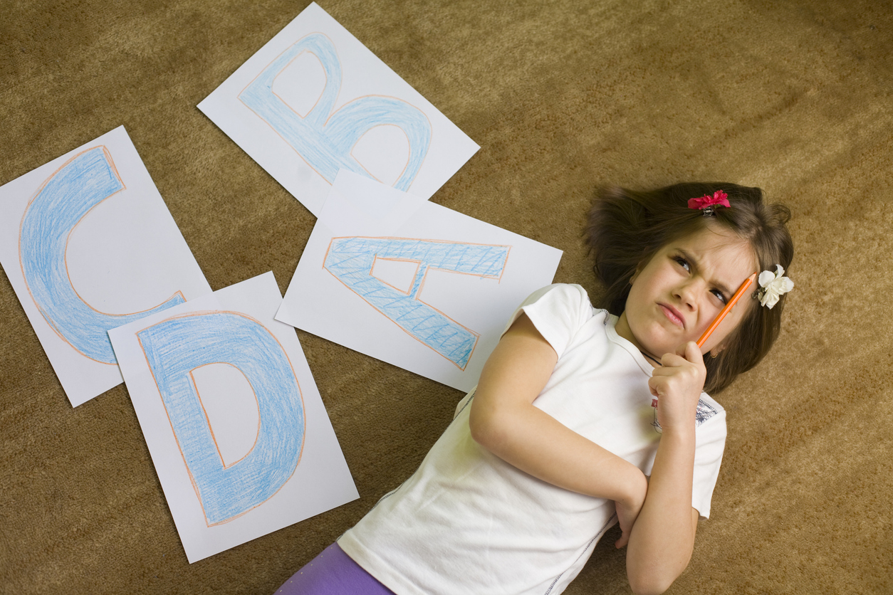 Preschool child thinking while learning letters with alphabet cards on the floor