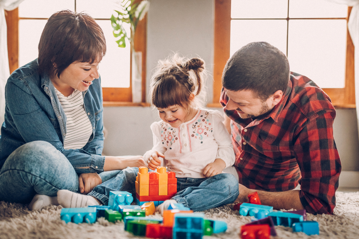 Parents playing with a young child using colorful building blocks during screen-free family time